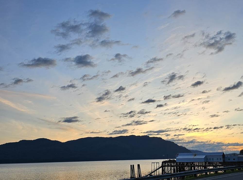 Sunset sky over the water in Hoonah, Alaska, with a wooden pier and waterfront buildings along the shore