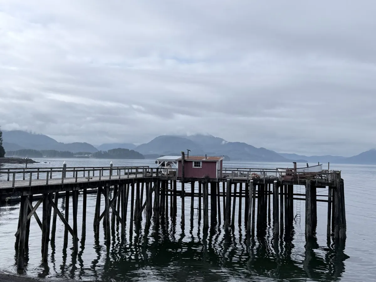 A weathered dock on pilings in Hoonah's harbor, with mountains across the strait